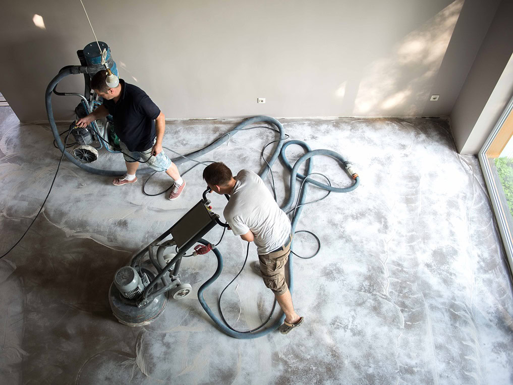 Two workers using floor polishing machines on a concrete surface in a well-lit office emphasize the importance of professional cleaning, office cleaning services kansas city