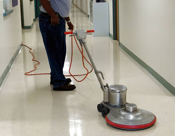 A person operates a floor buffer machine in a clean, empty hallway with shiny tile floors, showcasing effective workplace cleaning.